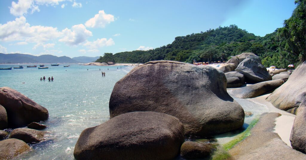 Campeche Island shoreline with granite boulders, clear turquoise water, white sand and forest, with boats anchored offshore